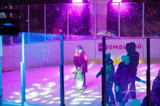 People skate in the evening on a lighted ice rink. A blizzard is raging and snow is falling. Zelenograd, Russia 28.01.2022.