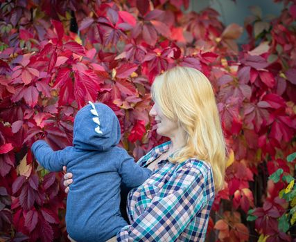 A young beautiful mother shows her baby red leaves on a bush. Walk in summer.