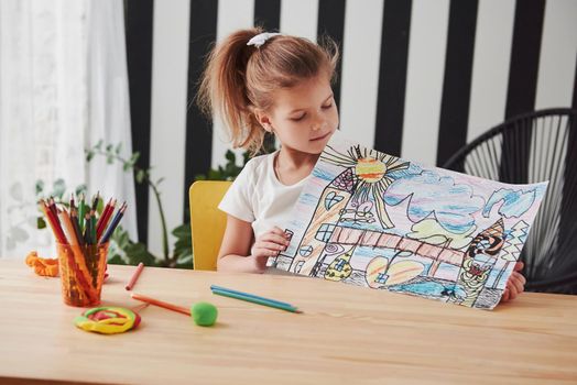 She will be professional painter one day. Cute little girl in art school shows her first picture drawn by pencils and markers.