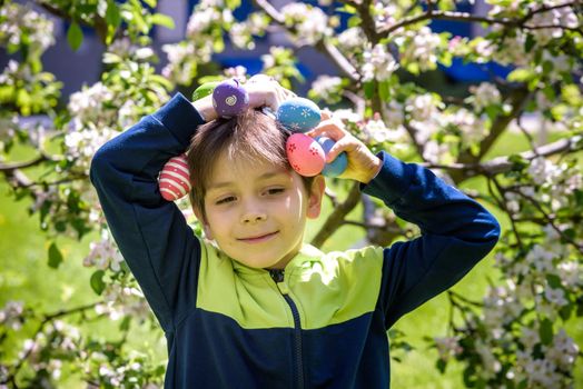 Different color Easter Eggs in a child's hands- egg hunt. Boy hold Easter eggs over his head. Cute smiling child on traditional play game on Easter.