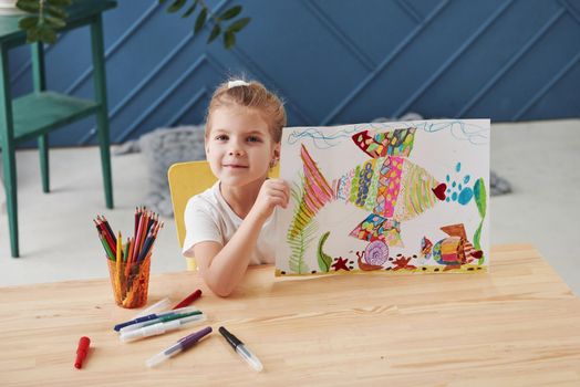 Good beginnings. Cute little girl in art school shows her first paintings drawn by pencils and markers.