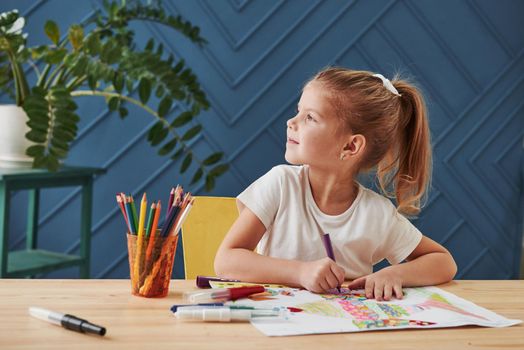 Looking to the side. Cute little girl in art school draws her first paintings by pencils and markers.