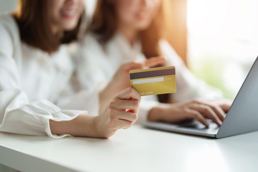 Two asian girlfriends shopping online with laptop computer and credit card at home.