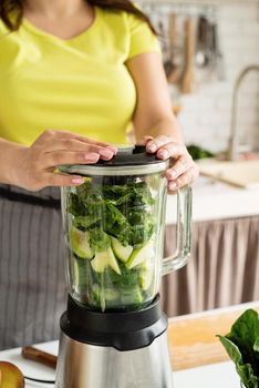 Preparing healthy foods. Healthy eating and dieting. Young brunette woman making green smoothie at home kitchen