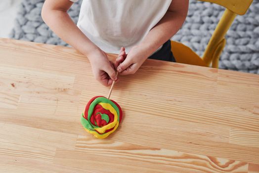 Showing off result of work. Children playing with colored plasticine on the wooden table at home.