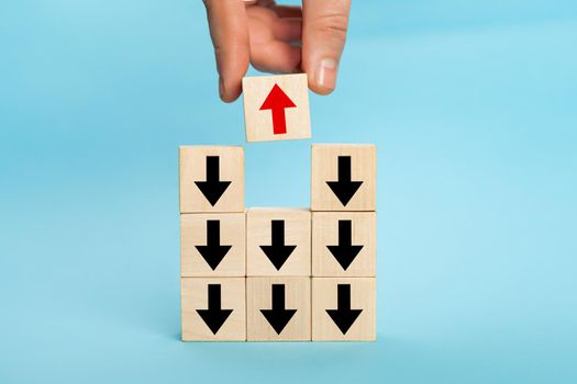 Businessman hand picked wooden block with red arrow facing the opposite direction black arrows, unique, think different, individual and standing out from the crowd concept, technology innovation,