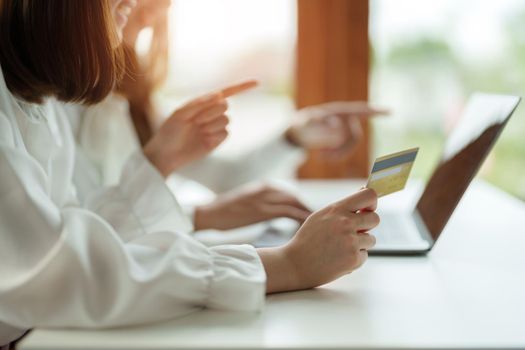 Two asian girlfriends shopping online with laptop computer and credit card at home.