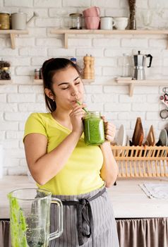 Healthy eating, dieting concept. Young brunette woman drinking green smoothie at home kitchen from mason jar