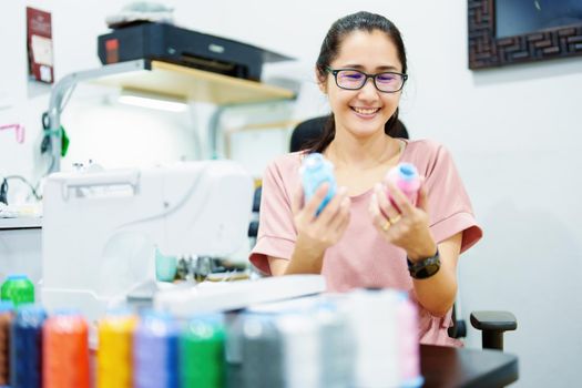 Embroidery, handicrafts, SME, family business Portrait of an Asian female designer picking up sewing threads for Design patterns using automatic embroidery machines according to customer orders