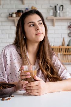 Alternative coffee brewing. young woman in lovely pajamas drinking coffee with milk at home kitchen