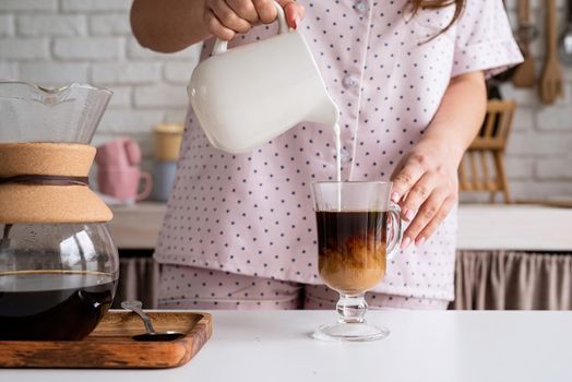 Alternative coffee brewing. young woman in lovely pajamas making coffee at home kitchen adding milk