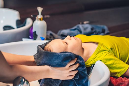 Wet Head Blond little Boy lie leaning on over sink. Woman female hands wipe hair with towel after wash. Beauty hairdressing salon Work. Child enjoy Barbershop Haircut. Kid client.