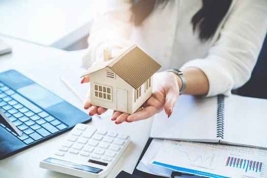 Accountant, businessman, real estate agent, Asian business woman handing model house to customers along with house interest calculation documents for customers to sign