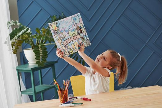 Admiring her creation. Cute little girl in art school shows her first paintings drawn by pencils and markers.