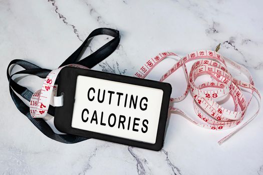 Cutting calories on black name tag with measure tap on white desk. Healthy and diet concept.