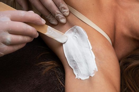 Cosmetologist in beauty clinic performs a epilation procedure for removing hair from the armpits using a white shugaring paste. Beauty and body care concept.