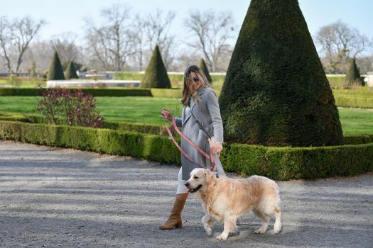 Stylish woman walking with a labrador on a leash in a park