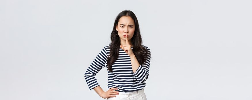 Lifestyle, people emotions and casual concept. Angry serious young asian woman scolding person being loud, shush with mad face and index finger pressed to lips, tell be quiet.