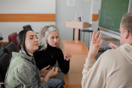 Two girls and a guy are talking in sign language. Three deaf students chatting in a university classroom