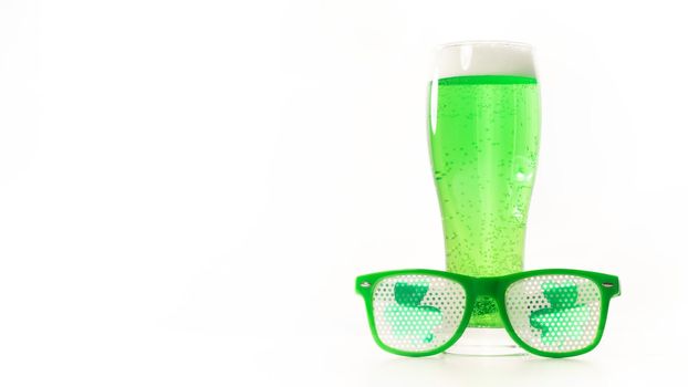 A glass of green beer and funny glasses for st patrick's day on a white background. Traditional Irish drink for a holiday. Copy spase