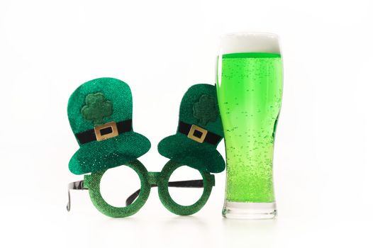 A glass of green beer and funny glasses for st patrick's day on a white background. Traditional Irish drink for a holiday.