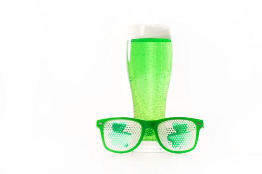 A glass of green beer and funny glasses for st patrick's day on a white background. Traditional Irish drink for a holiday. Copy spase