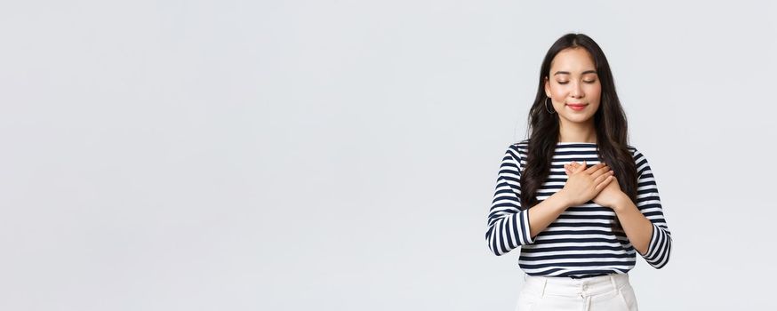 Lifestyle, people emotions and casual concept. Romantic tender korean beautiful girl close eyes and smiling, keep memory in heart, daydreaming or thinking about someone, touching chest.