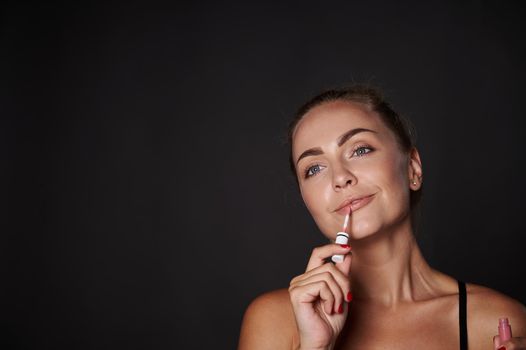 Natural beauty Caucasian middle aged woman applying moisturizing shining lip gloss. Make-up concept