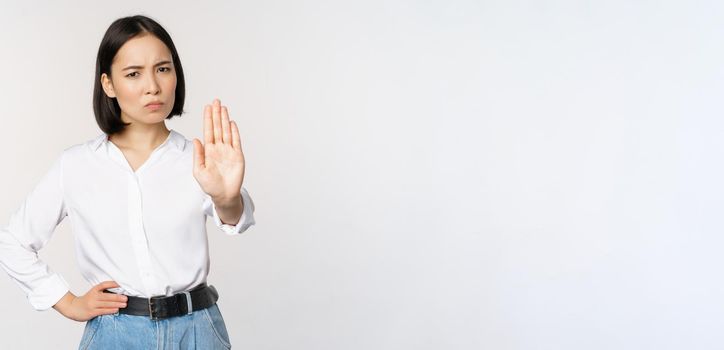 Portrait of young woman extending one hand, stop taboo sign, rejecting, declining something, standing over white background. Copy space