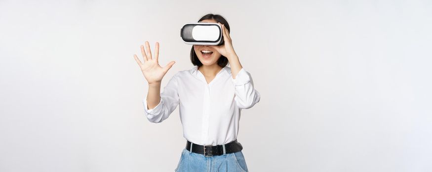 Vr chat. Asian girl saying hello in virtual reality glasses, smiling enthusiastic, concept of communication and future technology, white background.