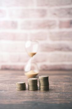 stack of coins and sand flowing through the bulb of sandglass.