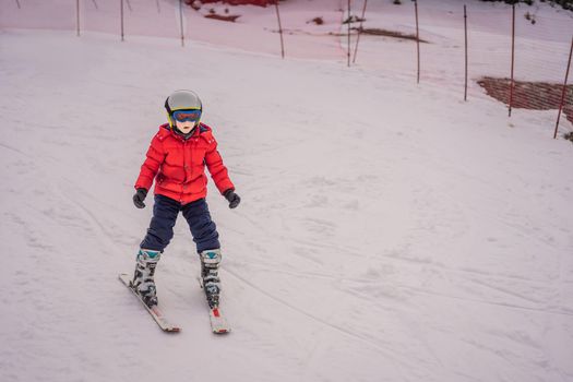 Child skiing in mountains. Active toddler kid with safety helmet, goggles and poles. Ski race for young children. Winter sport for family. Kids ski lesson in alpine school. Little skier racing in snow.