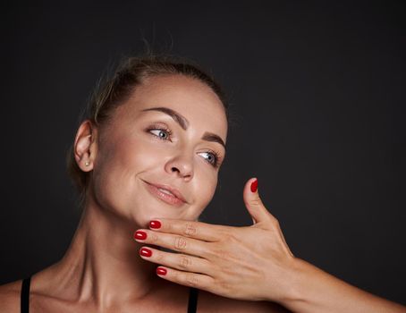 Close-up beauty portrait of a beautiful blonde European woman with clean, radiant tanned skin and well-groomed hands, isolated over black background. Cosmetology, youth concept for ads