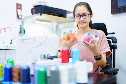 Embroidery, handicrafts, SME, family business Portrait of an Asian female designer picking up sewing threads for Design patterns using automatic embroidery machines according to customer orders