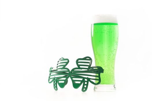 A glass of green beer and funny glasses for st patrick's day on a white background. Traditional Irish drink for a holiday. Copy spase