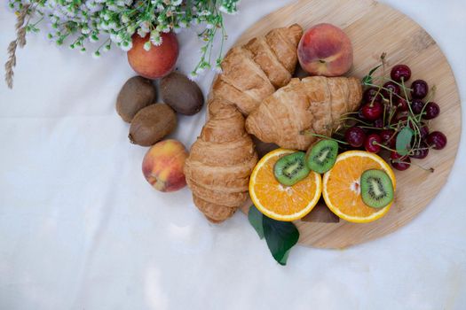 picnic in summer with snacks, fresh fruits and flowers. croissants, kiwi, orange, cherry. background top view mockup,a place for text.