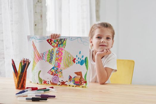 Nice daylight. Cute little girl in art school shows her first paintings drawn by pencils and markers.