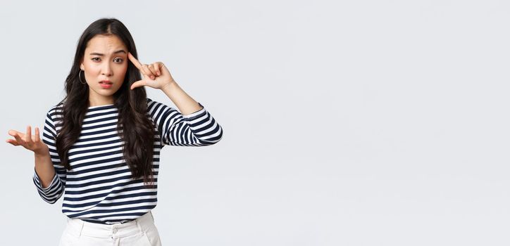 Lifestyle, people emotions and casual concept. Disappointed and annoyed young asian woman scold person making stupid mistake, roll finger over temple and raise hand in dismay.