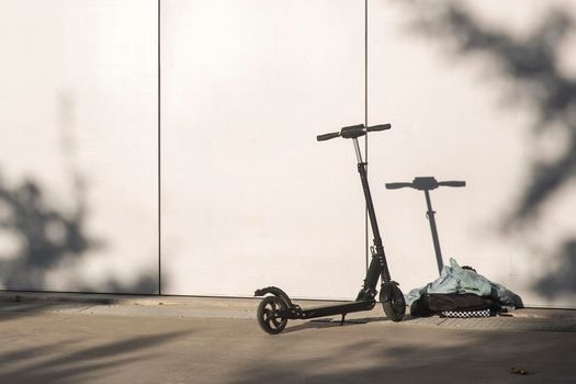 A black electric scooter is parked against the wall. The scooter casts a shadow on the wall