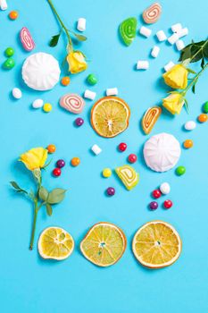 Marshmallows, candy, jelly beans, sweets , dry mugs oranges and yellow roses falling in wafer cone on a blue background. Copy space