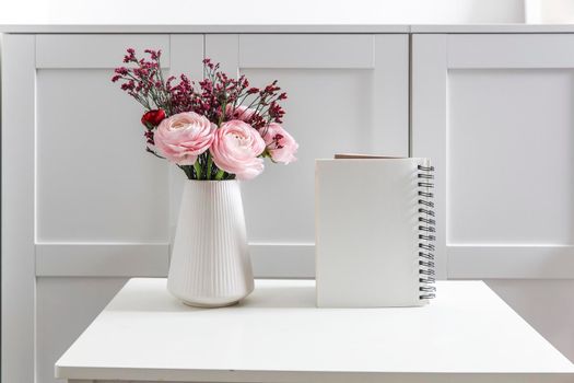 Bouquet of pink Persian buttercups on a white table in front of a chest of drawers. Scandinavian style. Place for text