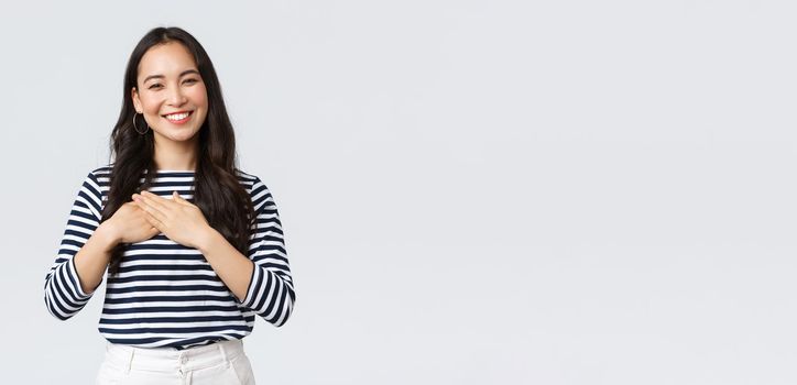 Lifestyle, people emotions and casual concept. Touched tender smiling asian woman gladly receive praises, hold hands on heart and grinning thankful, appreciate compliment.