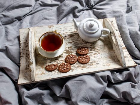 interior and home coziness concept. Top view. A cup of tea, a teapot with herbal tea, sugar bowl on a wooden white tray on the bed. Porcelain cup