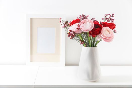 Bouquet of red and pink Persian buttercups on a white table. Scandinavian style. Place for text. Copy space