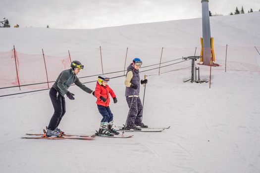 Mom and son are learning to ski with an instructor.Active toddler kid with safety helmet, goggles and poles. Ski race for young children. Winter sport for family. Kids ski lesson in alpine school. Little skier racing in snow.