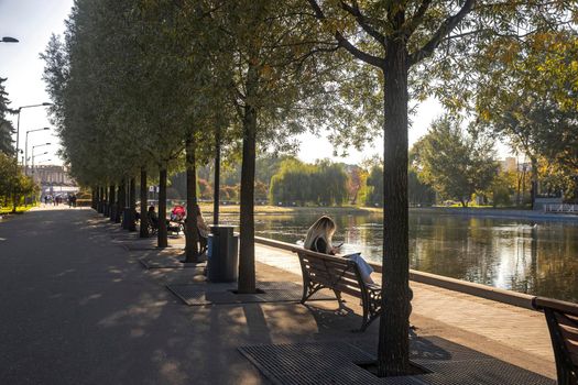 Moscow, Russia - 08 October 2021, Gorky Central Park of Culture and Leisure. A blonde girl sits on a bench near the pond, looks at the phone