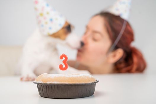 Caucasian woman congratulates her dog on the 3rd birthday. Jack russell terrier blows out the candle on the cake