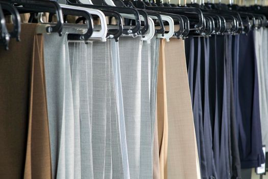 Men's gray and beige wool trousers hang on rails for sale in a store. Business style
