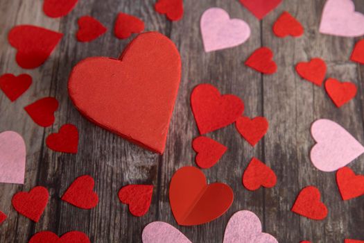 The red and pink paper and felt hearts of different shape and size are on a wooden brown table. The day of Valentine. Copy space