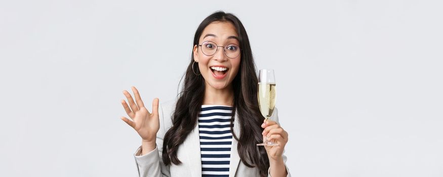 Business, finance and employment, female successful entrepreneurs concept. Friendly cheerful asian office worker enjoying party with colleagues, saying hi, drinking champagne and waving hand.
